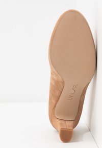 Chaussure à talon en daim beige à bout pointu montrée par la semelle avec le nom de la marque "unisa" et la taille 37 visibles en dessous.