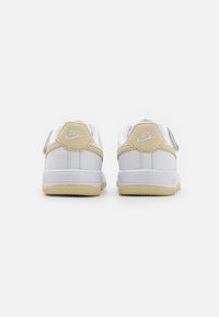 Weiße Nike-Sneaker mit gelben Akzenten, ausgestattet mit einem glatten Synthetik-Obermaterial, gepolstertem Schaft und strukturiertem Gummi-Außensohle.