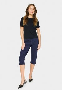 Black ribbed short-sleeve top paired with knee-length navy cropped pants and black slingback heels with bow accents. Simple, fitted design.