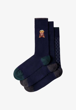 Tres pares de calcetines azul marino con diferentes colores en los dedos y el talón; uno tiene un pequeño oso con un suéter rojo a rayas y una "H" en el puño.