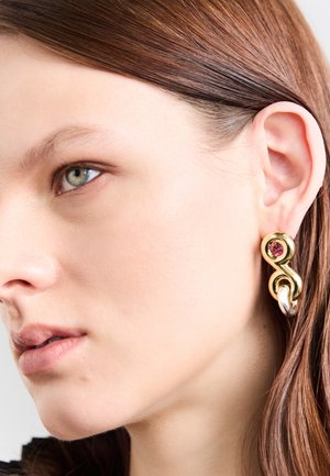 Ohrringe in Goldoptik mit einem gewundenen Design, die einen runden rosa Edelstein und einen glatten silbernen Akzent aufweisen. Strukturierten Oberfläche und gemischte Materialien.