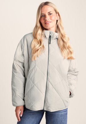 Light gray quilted jacket with a high collar and zip closure. Features a smooth texture and a relaxed fit, paired with casual denim.
