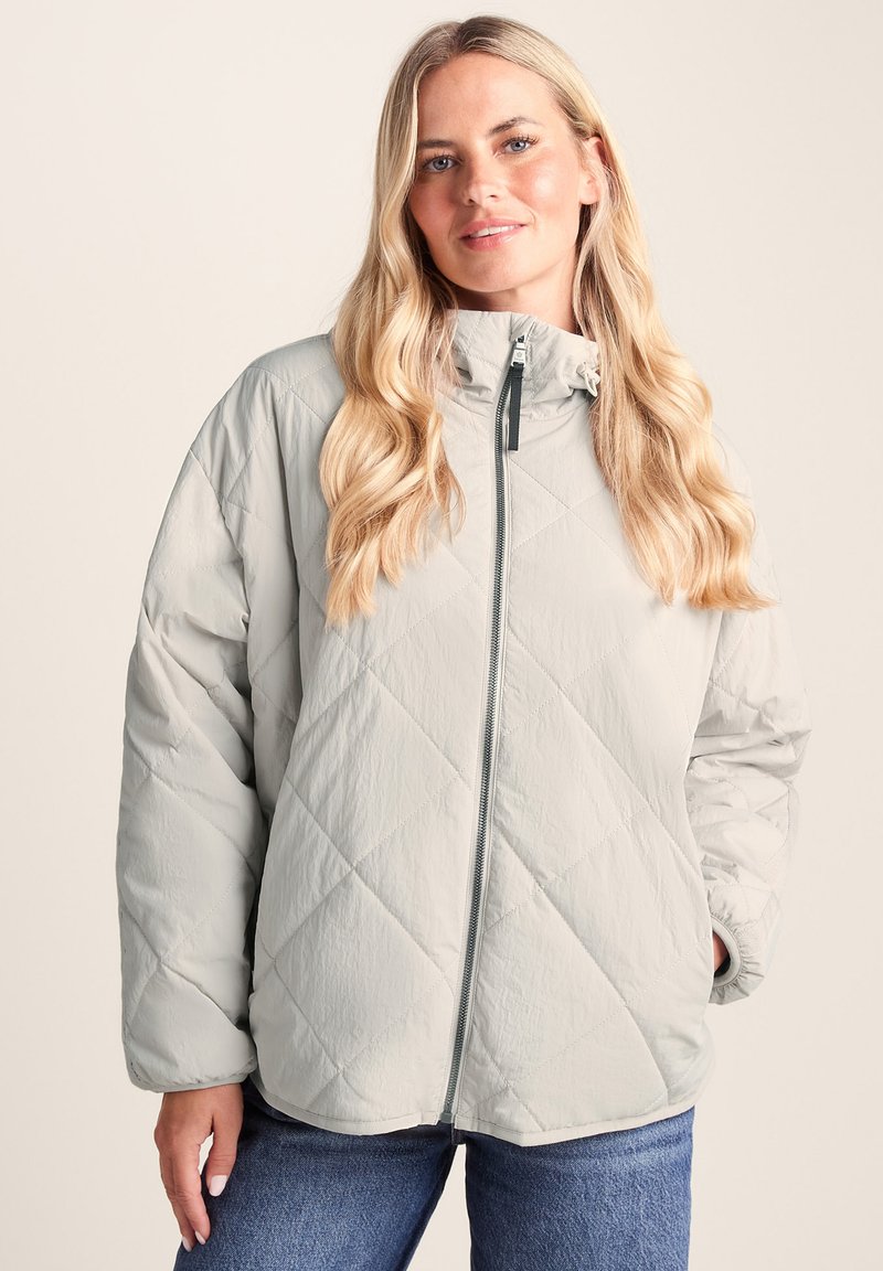 Light gray quilted jacket with a high collar and zip closure. Features a smooth texture and a relaxed fit, paired with casual denim.