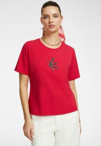 Maglietta di cotone rossa con maniche corte, caratterizzata da un design di insetto ricamato nero e colorato sulla parte anteriore. Vestibilità casual e scollo rotondo.