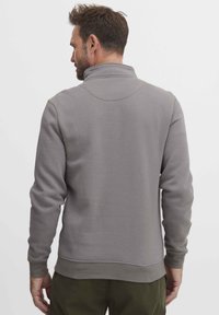 Felpa grigia con un colletto alto, design aderente, polsini e orlo a costine. Il tessuto appare morbido con una texture liscia. Nessun motivo visibile.