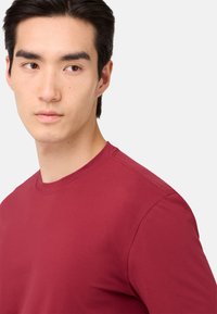 T-shirt di cotone bordeaux con scollatura a girocollo e maniche corte. Presenta una texture liscia e cuciture tonalità lungo le cuciture delle spalle.