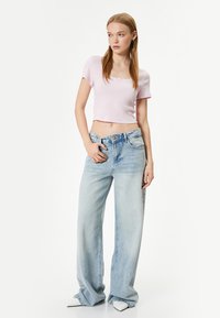 Roze geribbelde crop top met een vierkante halslijn en korte mouwen, gecombineerd met lichtblauwe wijdvallende jeans met een hoge taille en vervaagde accenten.