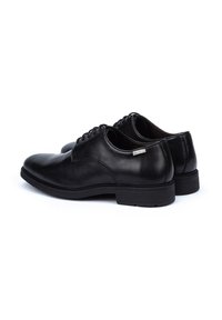 Chaussures de ville en cuir noir avec une finition lisse, bout rond, laçage à six œillets et un petit talon en caoutchouc. Détails de la marque subtils sur le côté.