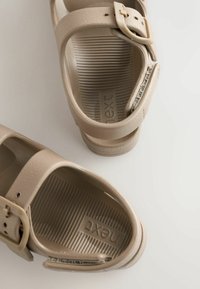 Beige sandalen met twee brede banden en een decoratieve gesp. Textuur in de binnenzool met geribd ontwerp. Logo "next" gegraveerd op het voetbed.