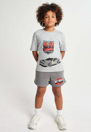 Child wearing grey Hot Wheels t-shirt with car graphic and matching grey shorts with Hot Wheels logo, standing with hands behind back.