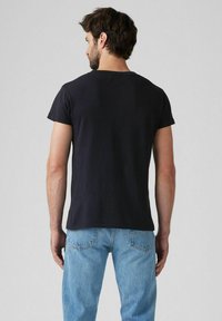 Black cotton t-shirt with short sleeves, rounded neckline, and a plain design, paired with blue jeans. Soft texture and casual fit.