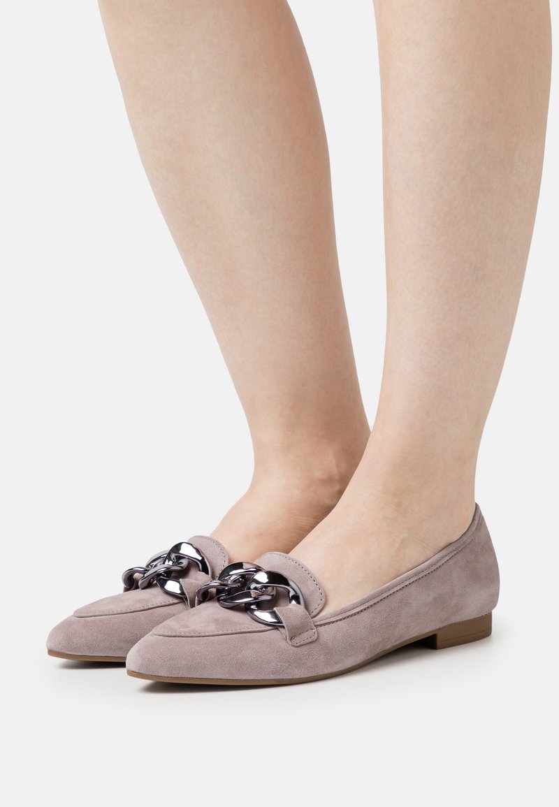 Mocassins pour femmes en daim mauve clair avec grand détail de chaîne noire, portés pieds nus, présentés sur un fond clair uni.