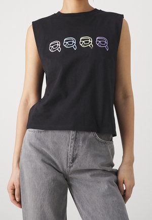 Camiseta sin mangas de algodón negra con cuatro rostros gráficos coloridos con gafas, distribuidos por el pecho. Combinada con jeans grises de cintura alta.