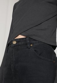 Jeans in denim nero con una vestibilità slim, dotati di un bottone dorato, dettagli di cucitura minimi e una superficie del tessuto texturizzata.