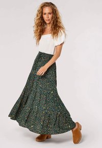 Floral maxi skirt in dark green with yellow and pink patterns; smocked waistband; paired with a white puff-sleeve top and tan clogs.