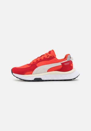 Roter und orangefarbener Puma-Sneaker mit weißem Seitenstreifen und klobiger weißer Sohle, seitlich auf grauem Hintergrund gezeigt.