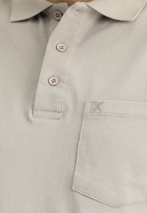 Hellbeige Poloshirt aus strukturiertem Stoff, mit drei Knöpfen und einer kleinen Tasche mit gesticktem Detail.