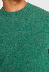 Grüner Strickpullover mit Rundhalsausschnitt. Strukturiertes Material mit einem melierten Muster, das verschiedene Grüntöne aufweist.