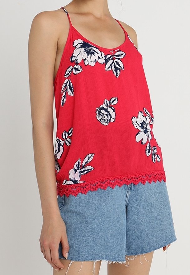 Top de tirantes espagueti de color rojo con estampados florales en blanco y azul, con un borde de encaje en la parte inferior, combinado con shorts de mezclilla.