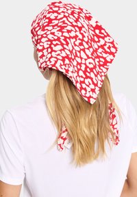 Eșarfă cu imprimeu leopard roșu și alb, formă triunghiulară, material ușor, legată la spate, căzând peste părul blond, purtată cu un tricou alb.