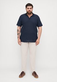 Navy polo shirt with vertical stripes, short sleeves, and a relaxed fit, paired with beige trousers and brown sneakers.