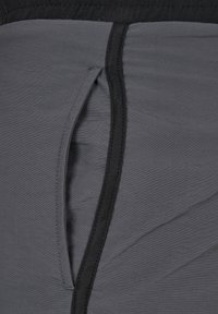 Tissu gris avec une texture douce, doté d'une taille noire et d'une ouverture de poche latérale, mettant en avant un design léger et élastique.