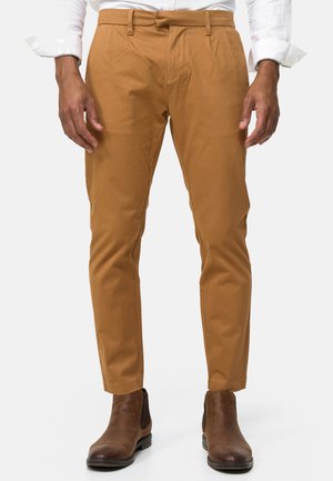 Chinos color marfil hechos de una mezcla de algodón, con un corte ajustado, frente plano y presillas para cinturón. Combinados con botas de cuero marrón hasta el tobillo.