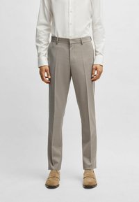 Pantaloni grigi chiari su misura con fronte piatto, leggero lucido e pieghe stirate. Indossati con una camicia bianca con bottoni e scarpe beige.