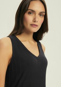 Czarny bezrękawnik z dekoltem w kształcie litery V, z pionowym prążkowanym wzorem i dopasowanym krojem. Gładki materiał i proste linie podkreślają sylwetkę.