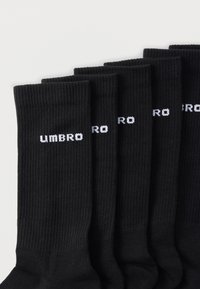 Černé bavlněné ponožky s hladkým žebrovaným vzorem, s bílým logem „UMBRO“. Šest párů úhledně srovnaných, s hladkým povrchem a jednotným designem.