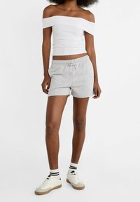 Grijze katoenen shorts met een verstelbare trekkoord taille, gecombineerd met een witte off-shoulder top en casual witte sneakers met zwarte accenten.