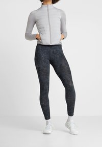 Ljusgrå zip-up jacka med strukturerad isolering och långa ärmar, kombinerad med mörka leggings med ett subtilt mönster och hög midja.