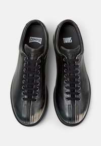 Mustat nahkaiset lenkkarit, joissa on sileä pinta, nyöritys, kontrastiväriset kärkikoristeet ja brändäys sisäpohjissa.