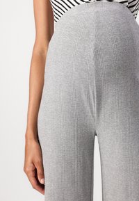 Graue gerippte Hosen mit einem elastischen Bund, die eine hohe Taille haben. Der Stoff hat eine weiche Textur mit vertikalen Linien.
