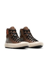 Bottes montantes marron en cuir et toile, avec des lacets noirs, des semelles en caoutchouc et des embouts texturés. Logo sur le côté.