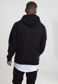 Felpa nera con cappuccio realizzata in tessuto morbido, dotata di tasca a marsupio, polsini a coste e vestibilità rilassata. Dettagli di cuciture visibili.