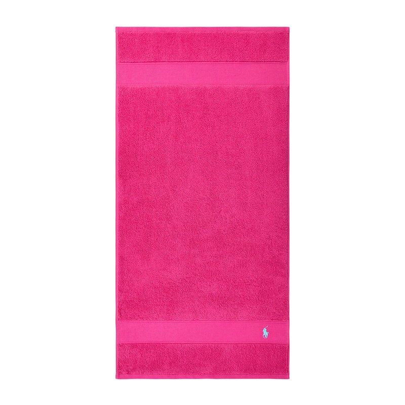 Ροζ βαμβακερή πετσέτα μπάνιου με ομοιόμορφη υφή, δύο οριζόντιες λωρίδες και μικρό μπλε λογότυπο στην κάτω δεξιά γωνία.