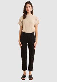 Haut beige texturé à manches courtes, pantalon noir ajusté à taille haute avec des plis, associé à des sandales tressées noires.