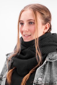 Black knitted scarf with a textured pattern, worn over a black top, paired with a denim jacket. Features a cozy, layered look.