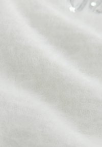 Tissu tricoté blanc avec une texture douce et duveteuse. La surface présente des fibres subtiles, avec un aspect lisse et légèrement réfléchissant.