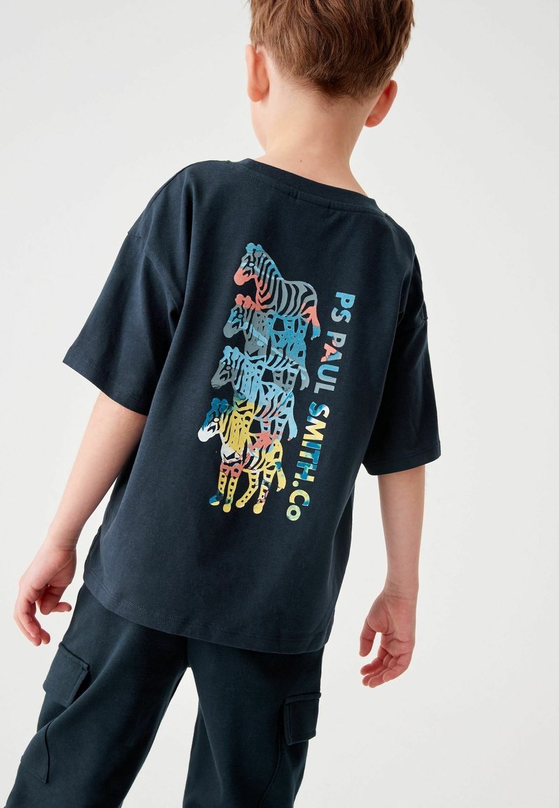 Enfant portant un t-shirt noir avec des zèbres colorés empilés verticalement et le texte "PS PAUL SMITH CO" dans le dos.