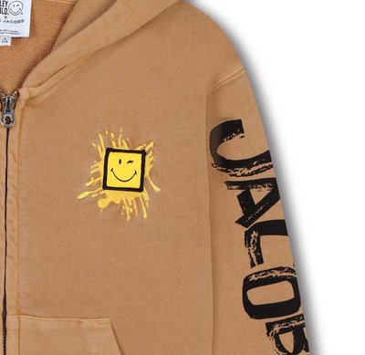 Felpa con cappuccio color sabbia con un design centrale di un sorriso giallo su uno spruzzo, caratterizzata da una grafica testuale nera lungo la manica.