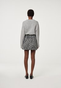 Grauer Strickpullover mit langen Ärmeln, kombiniert mit einem schwarz-grauen gemusterten Rock. Das Outfit wird mit schwarzen Schuhen mit Verzierungen abgerundet.