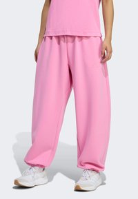 Ružové tepláky so voľným strihom a elastickými manžetami, vyrobené z jemnej látky, s bočnými vreckami a nenápadným logom značky na prednej strane.