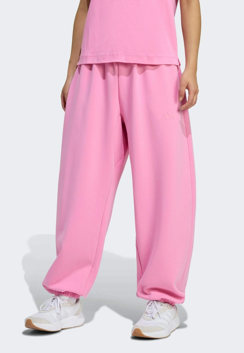 Ružové tepláky so voľným strihom a elastickými manžetami, vyrobené z jemnej látky, s bočnými vreckami a nenápadným logom značky na prednej strane.