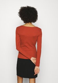 Žebrovaný top s dlouhým rukávem v barvě spálené oranžové, s širokým výstřihem a přiléhavým střihem, v kombinaci s černou minisukní.