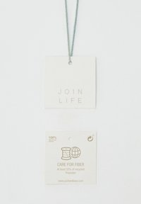 Étiquettes de vêtements avec les textes "JOIN LIFE" et "CARE FOR FIBER, at least 25% recycled polyester," attachées par une fine ficelle gris clair.