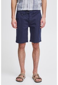 Shorts en coton bleu marine à coupe droite, avec deux poches avant et une fermeture à bouton, associés à des sandales texturées marron.
