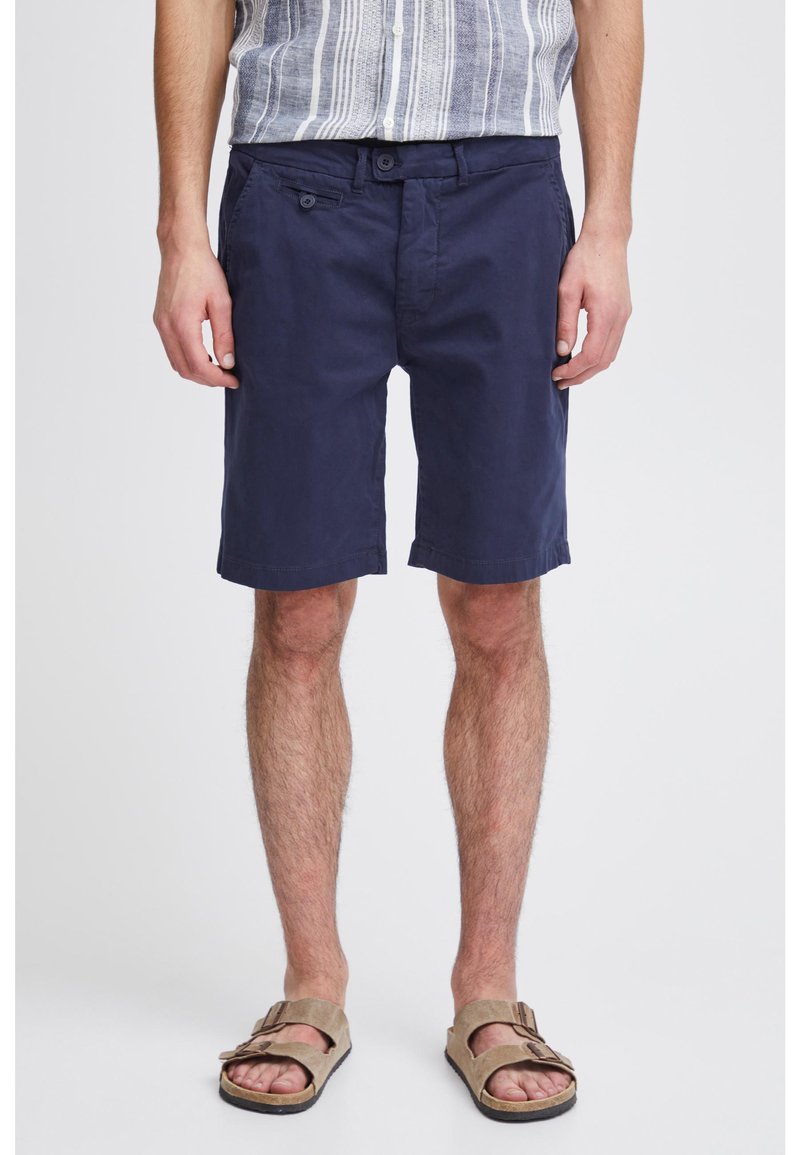 Shorts en coton bleu marine à coupe droite, avec deux poches avant et une fermeture à bouton, associés à des sandales texturées marron.
