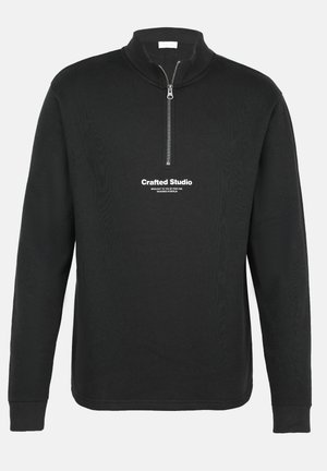 Musta vetoketjullinen pullover, joka on valmistettu tekstuurista kankaasta. Ominaisuuksiin kuuluu pitkät hihat, korkea kaulus ja etupuolella oleva valkoinen painettu teksti.